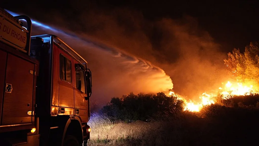Camion de pompiers luttant contre un feu de forêt la nuit.